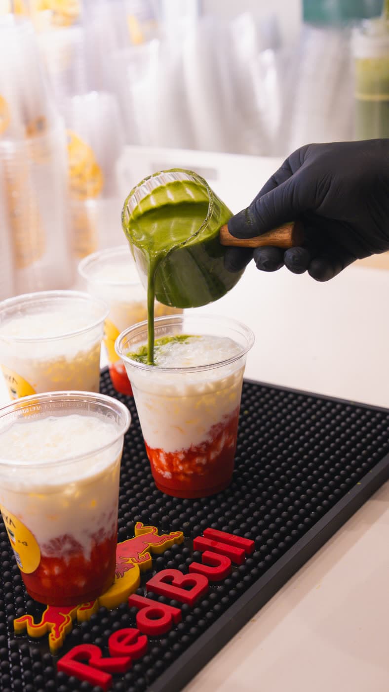 Matcha wird aus einem Krug in einen Becher mit Erdbeerschicht gegossen